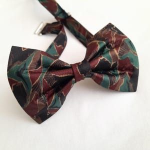 Puede incluir: Una pajarita marrón, verde y negra con estampado de camuflaje.