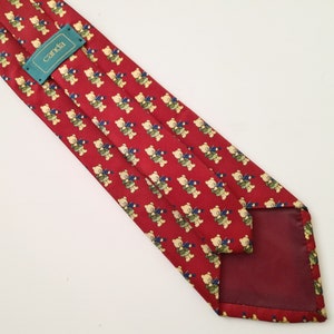 May include: Red silk tie with a pattern of small teddy bears playing musical instruments. The tie has a burgundy lining and a green label that says "canda".