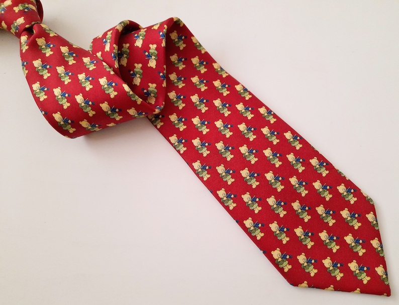 May include: A red silk tie with a repeating pattern of yellow teddy bears playing musical instruments.