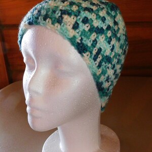 May include: A crocheted hat in shades of teal, blue, and white. The hat is made with a textured stitch and has a slouchy fit.