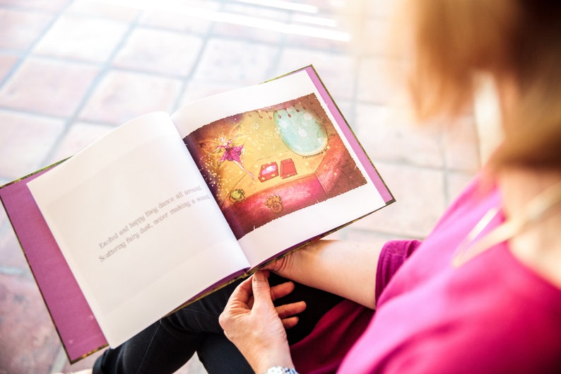 May include: A woman reads a book with a purple cover. The book is open to a page with an illustration of a fairy dancing in a room with a mirror and a few boxes. The text on the page reads "Each and every happy thing dance all around. Something they have never done, never making a sound."