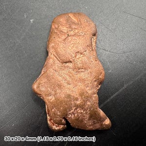 May include: A raw, irregular copper-coloured metal nugget with a textured, pitted surface. The object measures 30 x 20 x 4 mm. It features a metallic lustre with varied brown and reddish tones across its uneven, organic, and solid form.