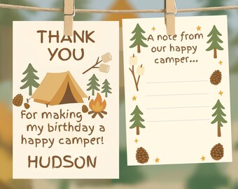 Op de afbeelding: Twee crèmekleurige kaarten met campingthema zijn aan een touwtje geklemd. Eén kaart leest "THANK YOU" en "For making my birthday a happy camper!" met een tent, kampvuur en bomen. De andere zegt "A note from our happy camper..." met lijnen om op te schrijven.