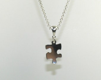 Puede incluir: Un collar de cadena de plata con un colgante de pieza de rompecabezas de plata.