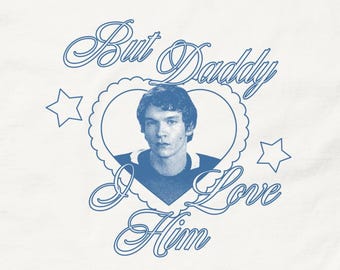 Pode incluir: Camiseta branca com um gráfico azul. O gráfico apresenta um retrato dentro de um coração, com o texto "But Daddy I Love Him" e estrelas. A camiseta é feita de um material macio.