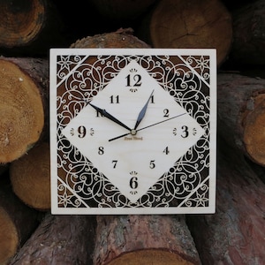 Puede incluir: Un reloj cuadrado de madera con un diseño decorativo e intrincado. La esfera del reloj es blanca con números y manecillas negros. El reloj está rodeado por un marco decorativo con un patrón floral.