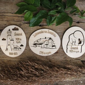 May include: Three wooden round ornaments with laser-cut designs depicting a mountaintop shelter, a tower, and an elephant. The ornaments feature the text "Schronisko na Śnieżniku", "Śnieżnik 1426 m n.p.m.", and "1899-1973".