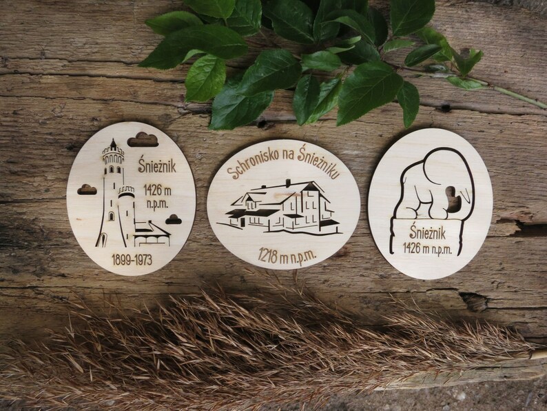 May include: Three wooden round ornaments with laser-cut designs depicting a mountaintop shelter, a tower, and an elephant. The ornaments feature the text "Schronisko na Śnieżniku", "Śnieżnik 1426 m n.p.m.", and "1899-1973".