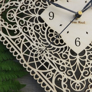 May include: A white wooden clock with a black filigree design and black hands. The clock face has black numbers and the text "Free Wood".