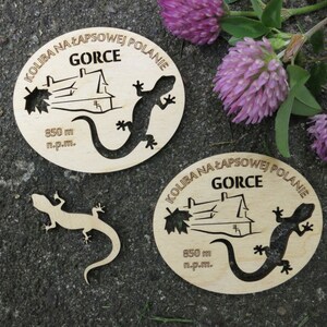 May include: Two wooden signs with the text "KOLIBA NA ŁAPSOWEJ POLANIE" and "GORCE" in Polish. The signs feature a house, a lizard, and the text "850 m n.p.m.".