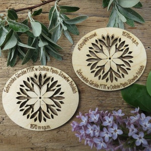 May include: Two wooden round signs with a laser-cut floral design. The signs are engraved with the text "Schronisko G&oacute;rskie PTTK w Dolinie Pięciu Staw&oacute;w Polskich" and "#StopWirusowi". The signs also include the text "1670 m n.p.m."