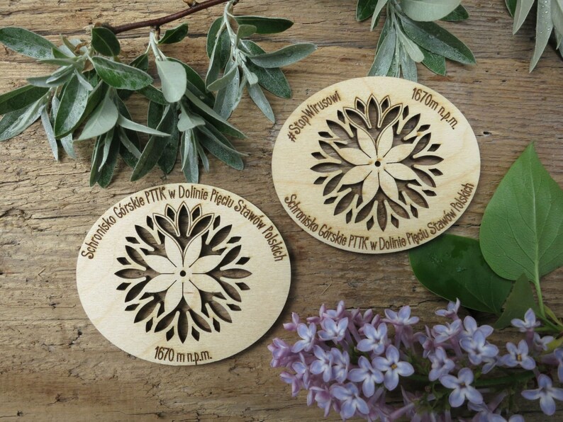 May include: Two wooden round signs with a laser-cut floral design. The signs are engraved with the text "Schronisko G&oacute;rskie PTTK w Dolinie Pięciu Staw&oacute;w Polskich" and "#StopWirusowi". The signs also include the text "1670 m n.p.m."