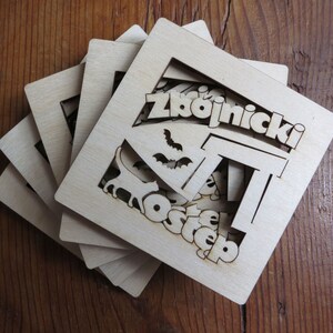 May include: A set of five wooden coasters with a laser-cut design featuring the words "Zbojnick&yacute; Ostep". The coasters are made of light brown wood and have a natural finish.