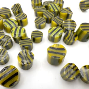 May include: A scattering of yellow and black striped sweets, resembling small logs, on a white surface. The sweets have a glossy finish and a cylindrical shape, with black stripes around a yellow base.