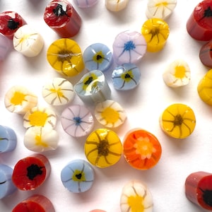 May include: A selection of colourful glass beads with flower designs. The beads are in various colours, including red, orange, yellow, blue, and white. Some beads are cylindrical, while others are round. The floral patterns feature detailed petals and centres.