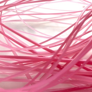 May include: A close-up of a bundle of pink and white plastic cords. The cords are tangled and overlapping, creating a textured and abstract pattern.
