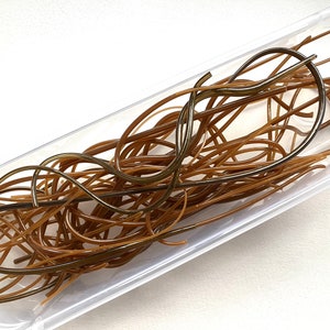 May include: A clear plastic container filled with brown and bronze-coloured flexible tubing. The tubing is arranged in a tangled, intertwined pattern, creating a textured appearance. The container is rectangular with slightly rounded corners.