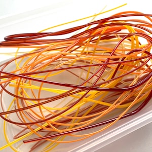 May include: A close-up of a pile of colourful, thin, flexible tubing in a clear plastic container. The tubing is in shades of yellow, orange, and red.