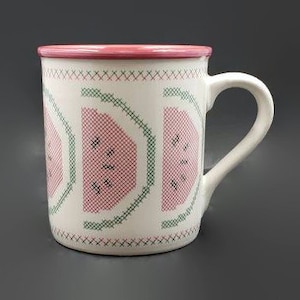 Può includere: Tazza in ceramica bianca con un bordo rosa e un design di anguria verde e rosa. Il design dell'anguria è stilizzato per assomigliare a un punto croce.