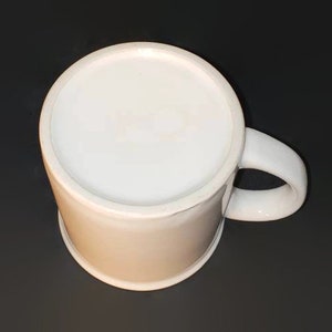 May include: A white ceramic mug with a simple design. The mug has a rounded handle and a smooth, white finish.