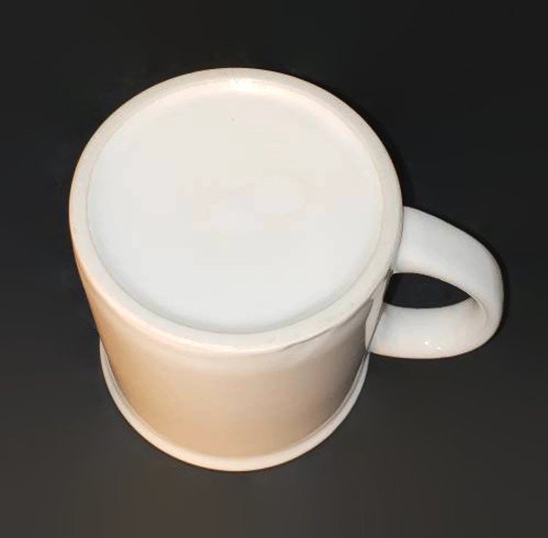 May include: A white ceramic mug with a simple design. The mug has a rounded handle and a smooth, white finish.