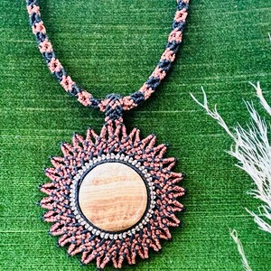 May include: A black and brown braided cord necklace with a round wooden pendant. The pendant is surrounded by a black and brown braided design.