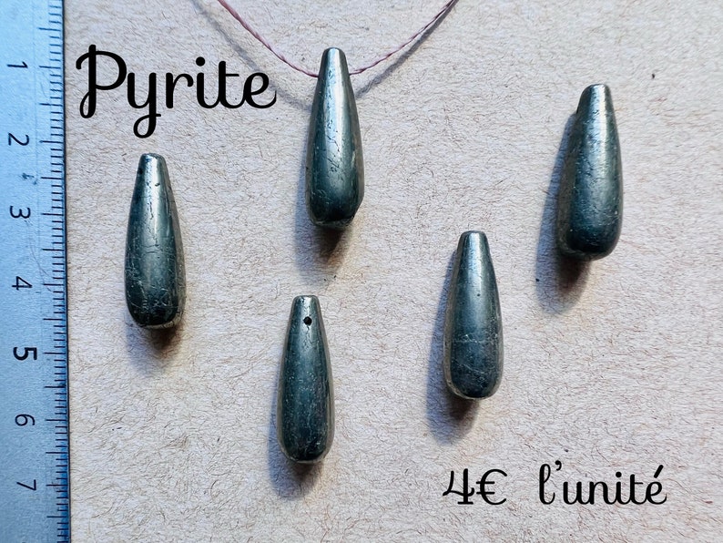 May include: Five elongated, teardrop-shaped pyrite pendants. The pendants are a metallic gray-green color and appear to be polished. The word "Pyrite" is written in a cursive font at the top of the image.