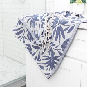 May include: A white bathroom vanity with a blue and white patterned towel folded on top. The vanity has two drawers and is in a bathroom with white tile.