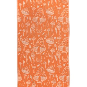 May include: Orange beach towel with a white mushroom pattern. The towel has a rectangular shape with a fringe on the short ends. The mushroom design includes various sizes and shapes of mushrooms.