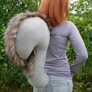 May include: A woman wearing a grey long-sleeved shirt and grey jeans with a grey and brown squirrel tail costume accessory attached to her back.