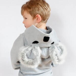 Op de afbeelding: Een lichtblauwe hoodie met een koala-ontwerp. De capuchon heeft zwarte vilt oren en een zwarte neus. De mouwen zijn afgewerkt met witte bont.