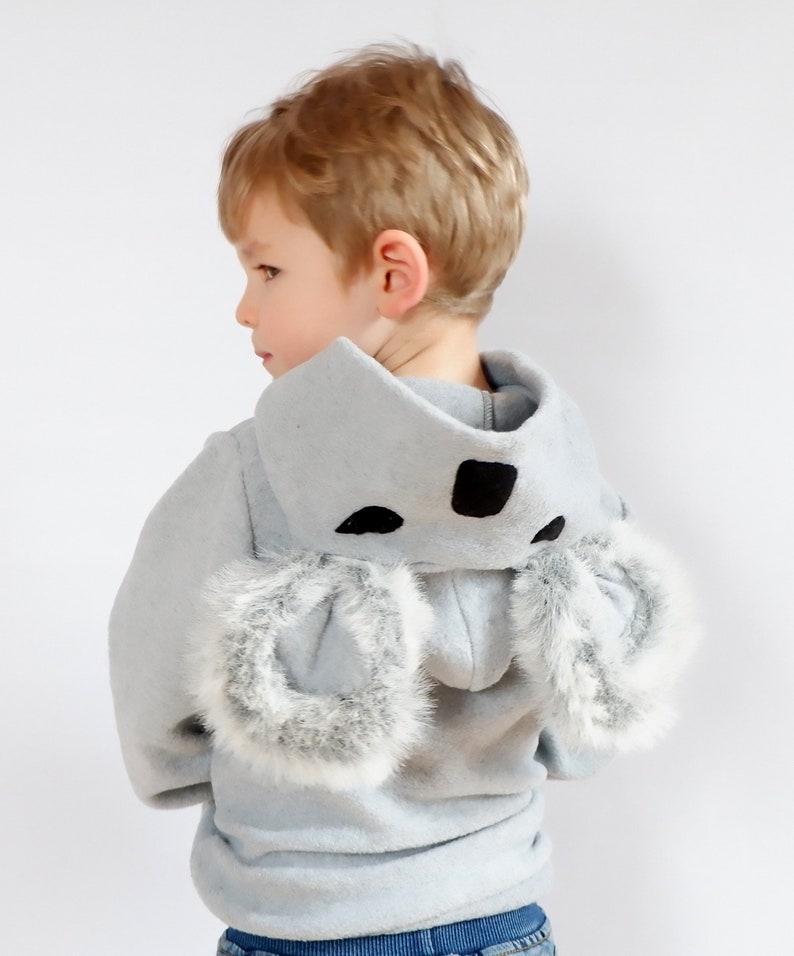 Op de afbeelding: Een lichtblauwe hoodie met een koala-ontwerp. De capuchon heeft zwarte vilt oren en een zwarte neus. De mouwen zijn afgewerkt met witte bont.