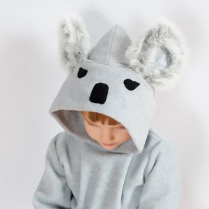 Op de afbeelding: Een grijze hoodie met pluche oren, een zwarte neus en zwarte ogen. De hoodie is ontworpen om eruit te zien als een koala.