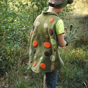 Puede incluir: Un disfraz de rana para niños, que incluye un chaleco verde adornado con círculos de fieltro de colores naranja, marrón y crema. El disfraz incluye una diadema a juego con ojos de rana y guantes.