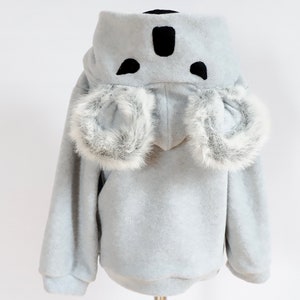 Op de afbeelding: Een lichtgrijs hooded sweatshirt met een koala-ontwerp. De capuchon heeft zwarte vilt oren en een neus, en de mouwen hebben witte nep bont trim.