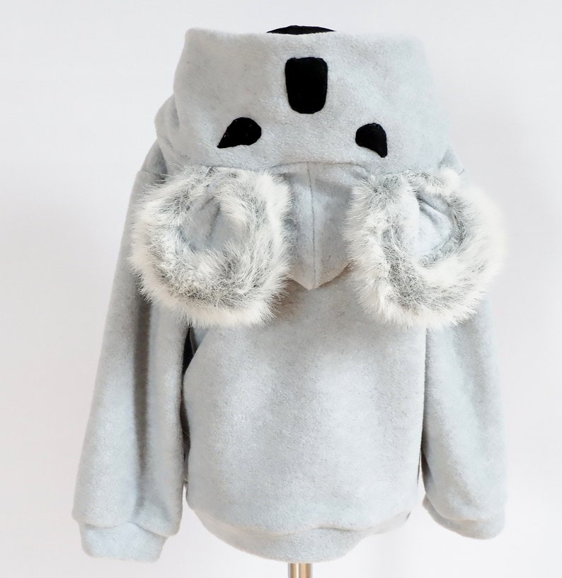 Op de afbeelding: Een lichtgrijs hooded sweatshirt met een koala-ontwerp. De capuchon heeft zwarte vilt oren en een neus, en de mouwen hebben witte nep bont trim.