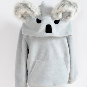 Op de afbeelding: Grijze fleece hoodie met een koala gezicht op de capuchon. De capuchon heeft twee harige koala oren.