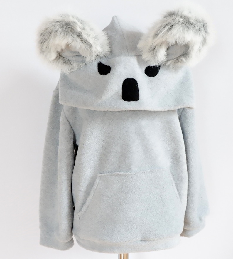Op de afbeelding: Grijze fleece hoodie met een koala gezicht op de capuchon. De capuchon heeft twee harige koala oren.