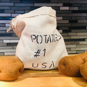 May include: A white burlap sack with the text "POTATOES #1 USA" printed on it. Two brown potatoes are in front of the sack.