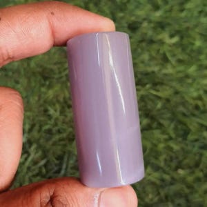 May include: A smooth, cylindrical object with a solid, light lavender-purple color. The item has a polished, glossy finish and a uniform, straight-sided shape, appearing as a small, solid, opaque component held between fingers.