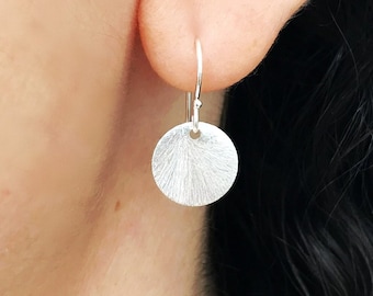 May include: Silver dangle earrings with a textured round disc pendant.