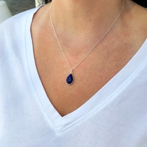 K&ouml;nnte beinhalten: Eine silberne Kettenkette mit einem tropfenf&ouml;rmigen Anh&auml;nger mit einem dunkelblauen Edelstein.