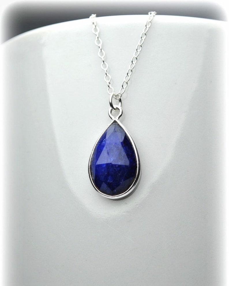K&ouml;nnte beinhalten: Eine silberne Kettenkette mit einem tropfenf&ouml;rmigen blauen Edelstein-Anh&auml;nger.