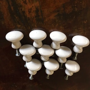May include: Ten white ceramic cabinet knobs with a rounded top and a screw-on base.