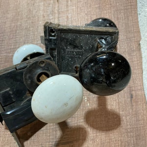 May include: Two antique door knobs with black and white porcelain handles. The knobs are attached to metal plates with keyholes. The plates have the text "Yale & Towne Mfg. Co. Stamford, Conn. U.S.A."