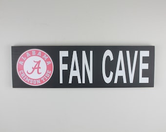 Puede incluir: Un letrero en blanco y negro con las palabras "FAN CAVE" en letras blancas. Un círculo rojo con la palabra "ALABAMA" y una "A" blanca en su interior se encuentra en el lado izquierdo del letrero.
