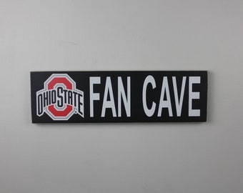 May include: Black and white sign with the Ohio State University logo and the text "FAN CAVE" in white letters.