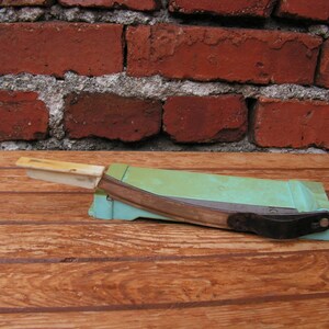 May include: A vintage green and white paper cutter with a metal blade. The cutter is sitting on a wooden surface.
