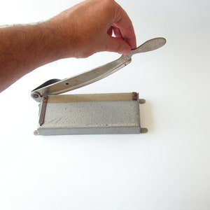 May include: A silver paper cutter with a metal base and a lever handle. The cutter is open and ready to cut.