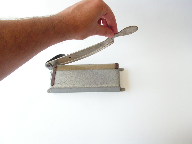 May include: A silver paper cutter with a metal base and a lever handle. The cutter is open and ready to cut.